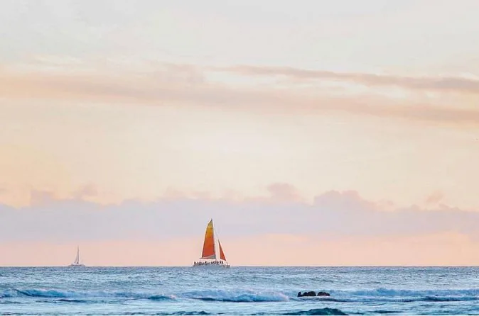 A catamaran with an orange sail on a calm sea at sunset